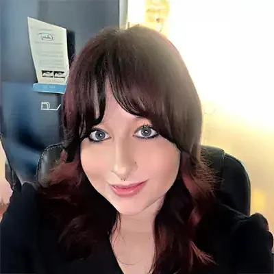 Close-up portrait of a person with dark shoulder-length hair seated at a desk chair indoors